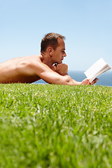 Image showing Man, book and reading on lawn in summer by ocean with knowledge, relax and information on vacation. Person, thinking and novel on grass with ideas, topless and outdoor for holiday by sea in Naples