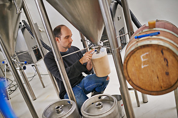 Image showing Brewery, man and container machine with craft beer for sample, alcohol test and production process in factory. Industrial hops, worker and working in distillery with jug for brewing in warehouse