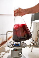 Image showing Hands, beaker and liquid at brewery for beer production with formula, gas burner and process. Person, worker and glass container for fluid on flame in industrial workshop for alcohol manufacturing