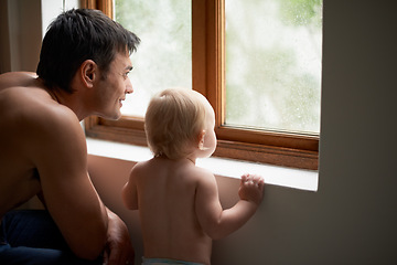 Image showing Rain, window and father with baby in a house for bonding, playing or having fun in their home together. Water, glass or dad with curious kid watching storm, weather or raindrops for learning or games