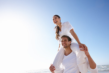 Image showing Happy, couple and beach with piggyback and blue sky for valentines day, love or summer holiday together in embrace or outdoor romance. Man and woman with smile by ocean in nature on mockup space