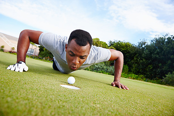 Image showing Black man, golf ball and cheating on golf course for competition with greenery, grass and concentration. Male person, fitness and blowing for activity with sportswear, professional and train outside