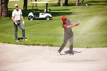 Image showing Men, stroke and golf ball in bunker on summer day for sports, health or exercise outdoor in activewear. People, training and playing game of nine holes on natural turf athlete in sand swinging club