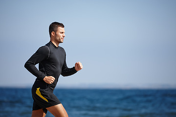 Image showing Man, running and blue sky by ocean for cardio with fitness goals, exercise and health workout. Male person, training and nature at beach with sports athlete for wellness, strong body and endurance