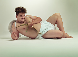 Image showing Humor, cupid and portrait of man with costume in studio for wings, bow and arrow on gray background. Fantasy, love and plus size male model lying down for role play, creative dress up or cosplay