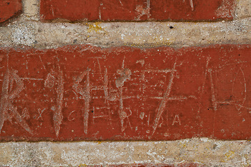 Image showing Building, writing and closeup of red, brick wall for texture, background and pattern of exterior structure. Architecture, construction and surface of material, concrete and cement for decoration