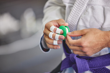 Image showing Brazilian jiu jitsu, hands and person with tape in gym for training, fitness or professional fighting sport. Injury, protection and martial arts athlete with gi, safety for fingers or workout in dojo