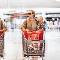 Image showing Mother shopping with his kid in the mall. Mother pushing shopping cart while holding and carrying her toddler baby boy child along mall corridor.