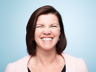 Image showing Comic model, portrait and happy with crazy face, positive and fun for comedic relief. Mature woman, blue background and joyful for healthy teeth, upbeat and excited with goofy look for laughter