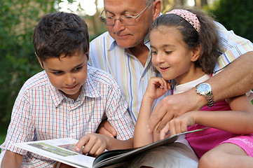 Image showing Grandfather and kids reading book outdoors