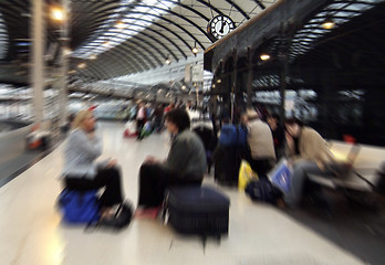 Image showing Zoom blurred image of people waiting for trains on Newcastle-upon-Tyne central station, UK, the zoom centred on station clock showing one o'clock 13.00 hrs