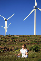 Image showing young blond woman doing yoga on the grass on a wind farm beneath