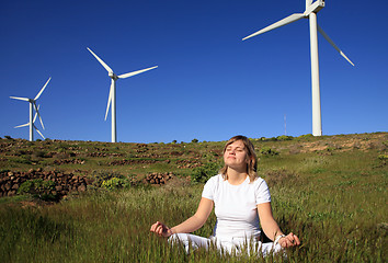 Image showing young blond woman doing yoga on the grass on a wind farm beneath