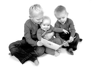 Image showing Two young brothers reading for their baby sister