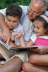 Image showing grandfather and kids reading book outdoors