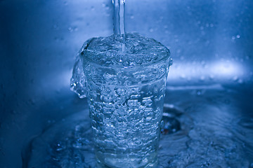 Image showing Water flowing in glass in dark blue tones