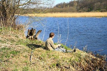 Image showing Fisherman sitting on the river shore