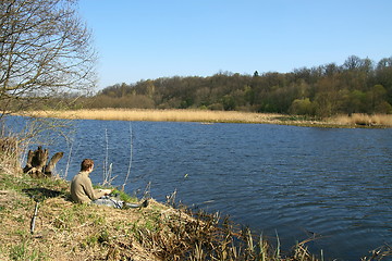 Image showing Fisherman sitting on the river shore