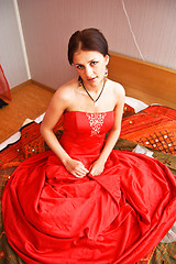 Image showing Attractive woman in red dress sitting on the bed