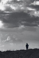 Image showing Monochrome lone walker (female) against large menacing sky, with slight added film grain for effect.