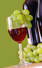 Image showing Red wine with grapes cluster over green