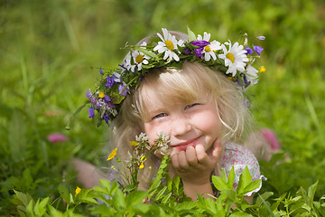 Image showing happy little girl in flowers wreath lying on green grass