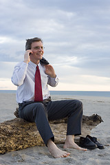 Image showing Smiling businessman making a phone call on a beach