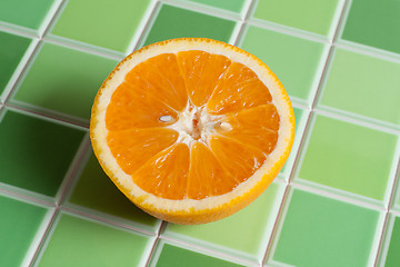 Image showing Half of the juicy orange on green tiled bar