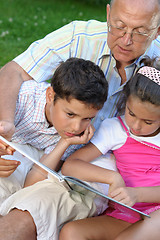 Image showing Grandfather and kids reading book outdoors