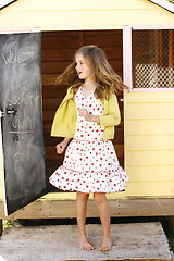 Image showing Pretty young girl spinning around outside her playhouse.