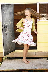 Image showing Pretty young girl spinning around outside her playhouse.