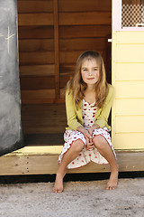 Image showing Portrait of a pretty young girl sitting outside her playhouse.