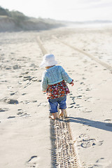 Image showing Little girl walking along a tire track on a beach. 