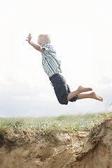 Image showing Young boy jumping off a sand dune.