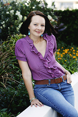 Image showing Portrait of a beautiful woman sitting on a fence.