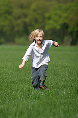 Image showing little, blond boy laughing and running through a meadow