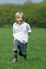 Image showing blond boy laughing and running through a meadow