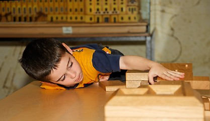 Image showing Cute little boy plays with wooden bricks and builds a house