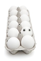 Image showing Funny egg with eyes among dozen in a paper box