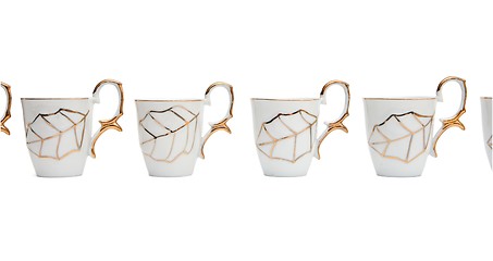 Image showing Row of white coffee cups with golden leaf isolated 