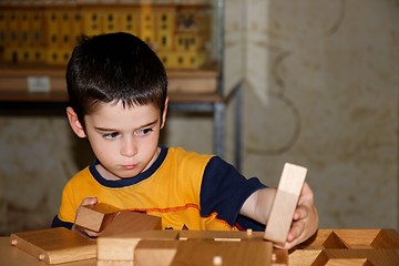 Image showing Cute little boy plays with wooden bricks and builds a house