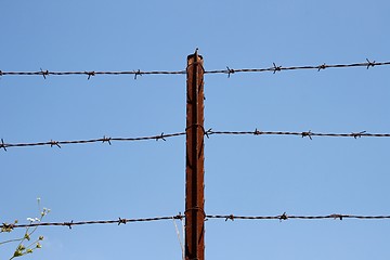 Image showing Three strands of barbed wire on rusty post over sky  background