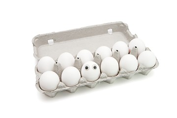 Image showing Funny egg with eyes among dozen in a paper box isolated
