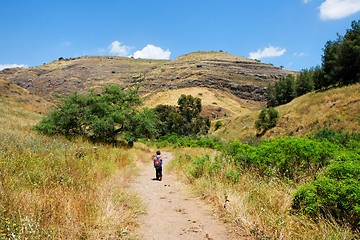 Image showing Small boy walks along a countryside road toward yellow autumn hills 