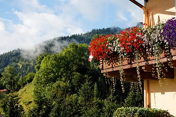 Image showing Alpine chalet balcony with flowers  on green hills background