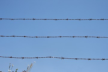 Image showing Three rusty strands of barbed wire over blue sky background