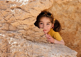 Image showing Cute little girl hides behind a rock