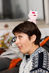 Image showing Young woman with a doll on her head sticks out her tongue 