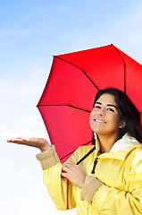 Image showing Beautiful young woman in raincoat with umbrella checking for rain