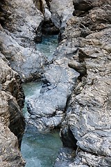 Image showing Narrow mountain stream flows among blue striped rocks